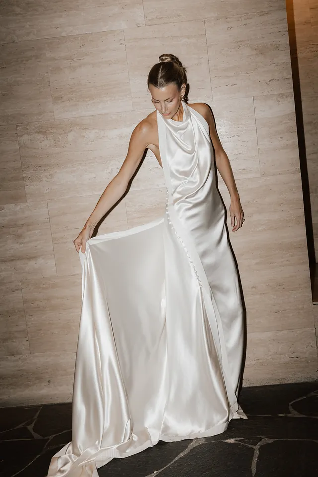 Clare looking down at her flowing ivory dress beside a warm stone wall at The Calile.